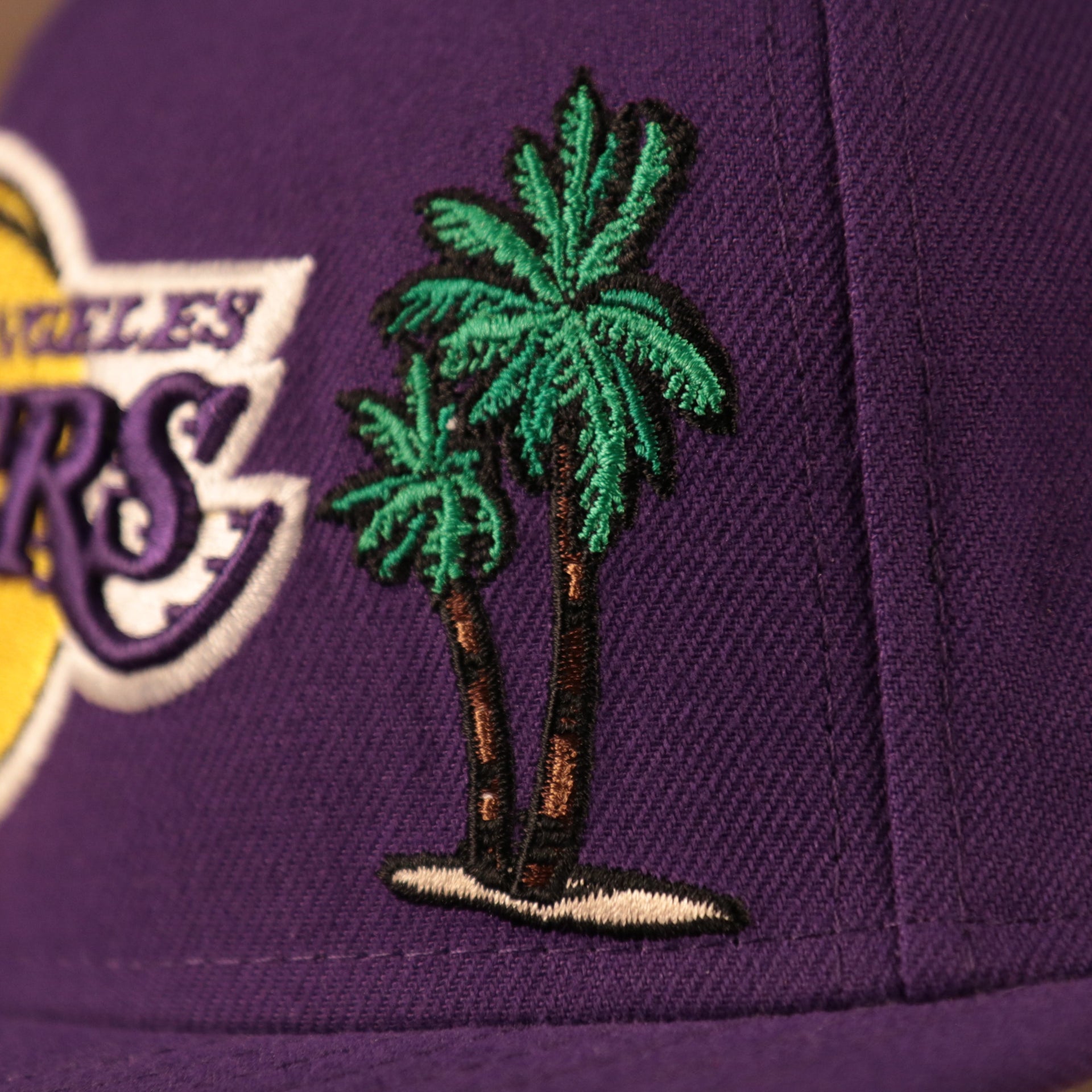 A close up of the palm tree patch on the front side of the purple Los Angeles Lakers 5950 all over patch fitted cap by New Era.