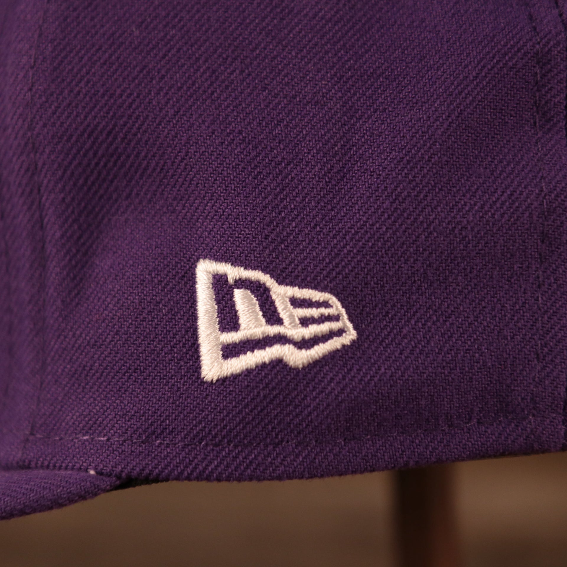 A close up shot of the white New Era logo embroidered on the left side of the purple Los Angeles Lakers gray bottom brim retro 5950 all over patch fitted hat.