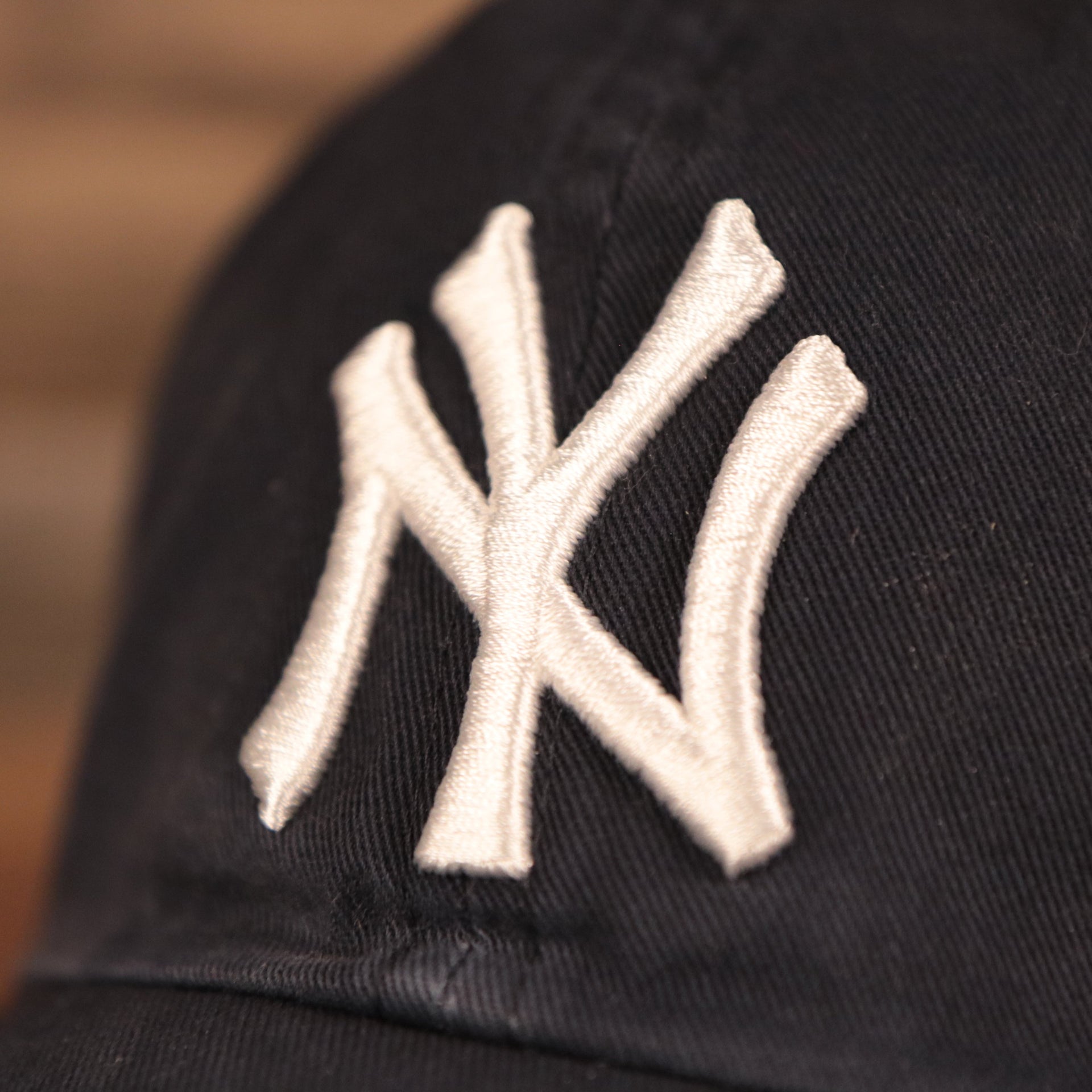 The white Yankees logo on the front of the navy blue cotton pink bottom dad hat.