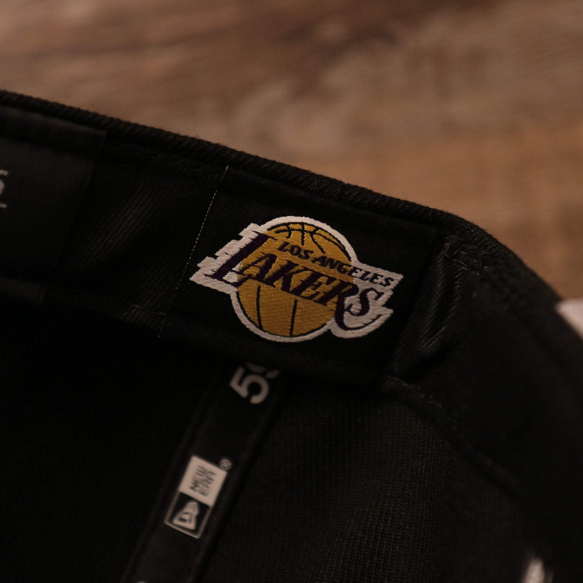 The Los Angeles strap on the inside of the gray bottom brim of the black 17x Lakers champs hat by New Era.