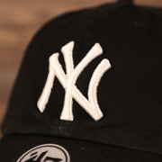 The white New York Yankees logo on the front side of the pink bottom baseball hat.