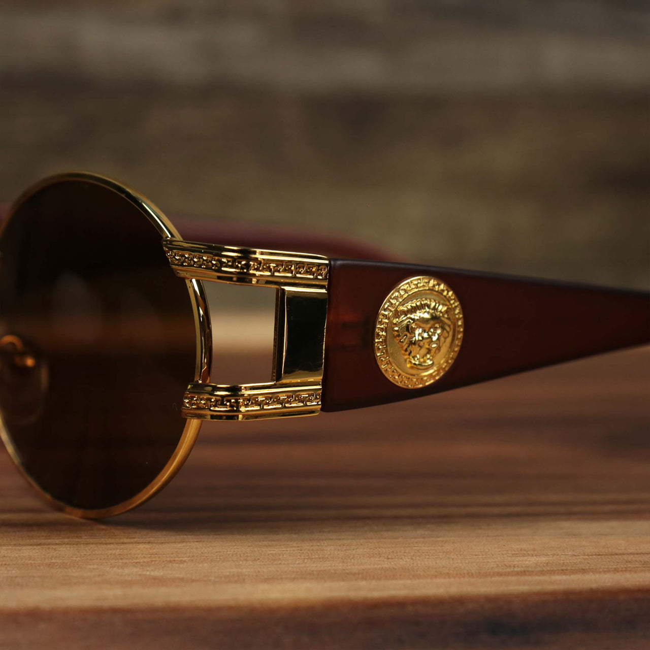 A close up of the hinge and lion head emblem on the Circle Frame Lion Head Emblem Brown Lens Sunglasses with Gold Frame