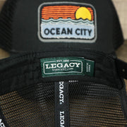 The Legacy Tag on the Youth New Jersey Ocean City Sunset Mesh Back Trucker Hat | Black And Black Mesh Youth Trucker Hat