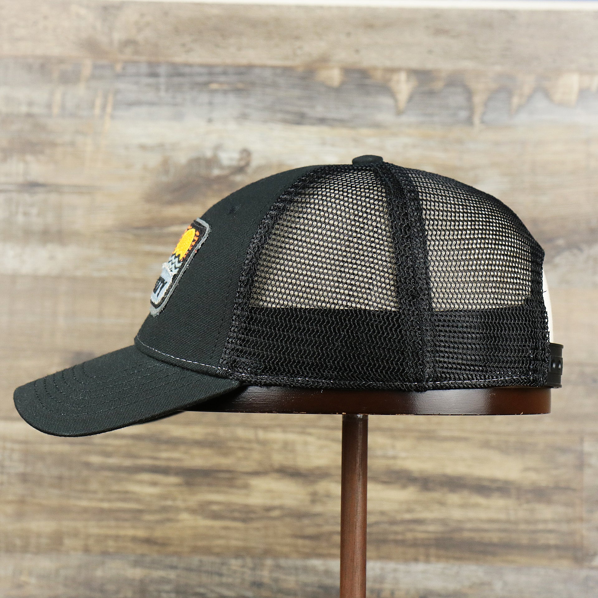 The wearer's left on the Youth New Jersey Ocean City Sunset Mesh Back Trucker Hat | Black And Black Mesh Youth Trucker Hat