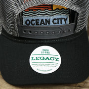 The Legacy Sticker on the Youth New Jersey Ocean City Sunset Mesh Back Trucker Hat | Black And Grey Mesh Youth Trucker Hat