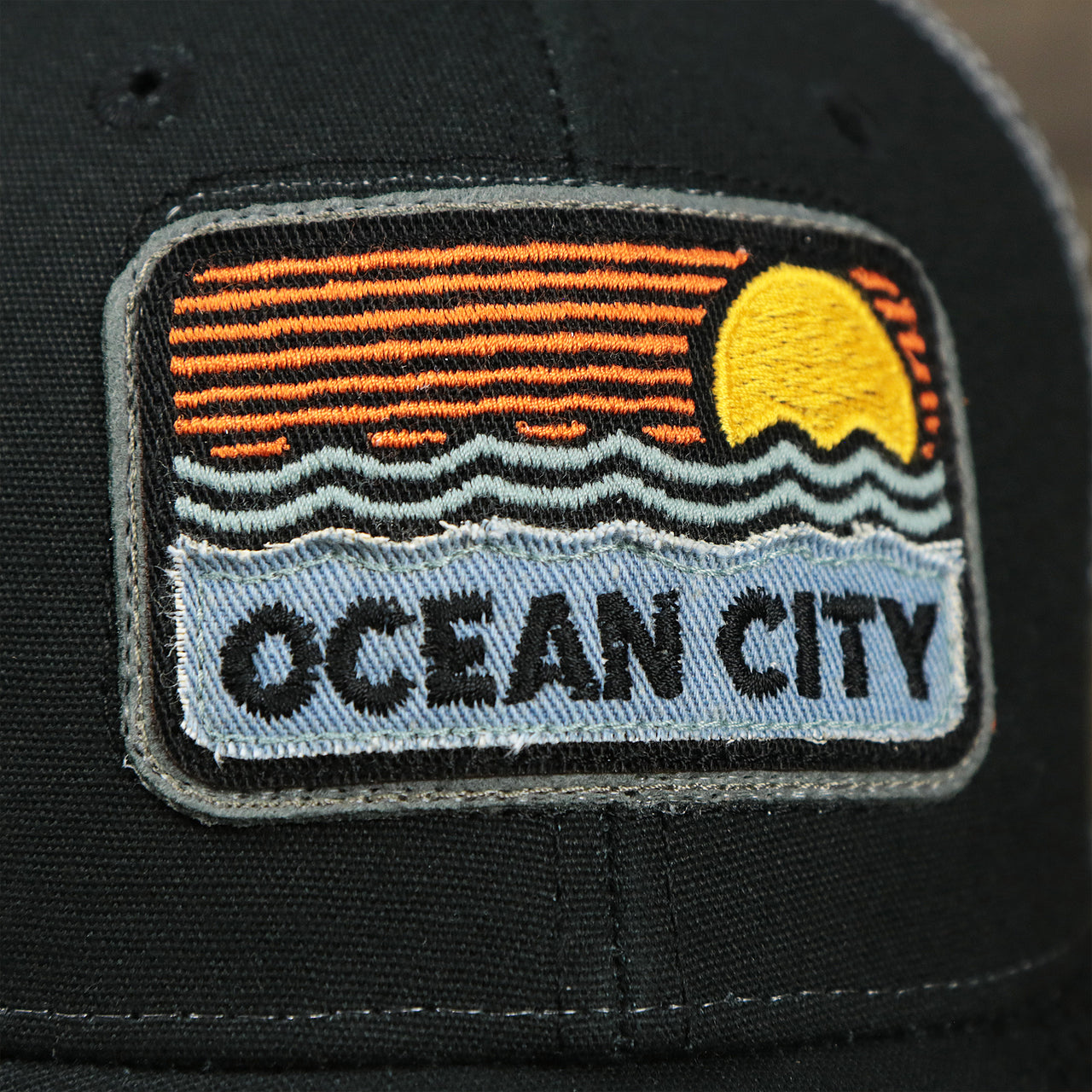 The Ocean City Sunset Patch on the Youth New Jersey Ocean City Sunset Mesh Back Trucker Hat | Black And Grey Mesh Youth Trucker Hat