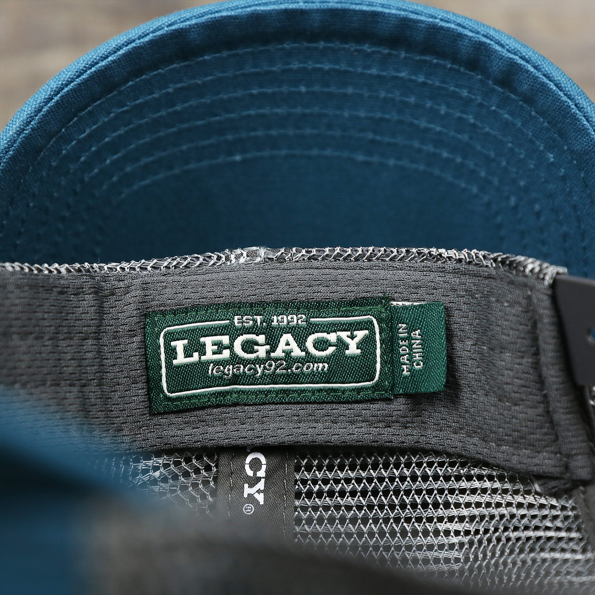 The Legacy tag on the Youth New Jersey Ocean City Sunset Mesh Back Trucker Hat | Marine Blue And Dark Gray Mesh Youth Trucker Hat