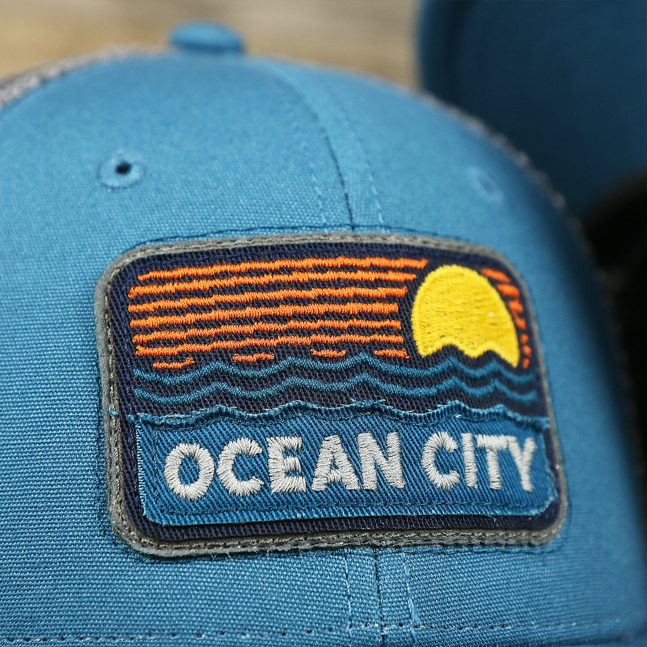 The Ocean City Sunset Patch on the Youth New Jersey Ocean City Sunset Mesh Back Trucker Hat | Marine Blue And Dark Gray Mesh Youth Trucker Hat
