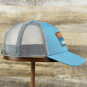 The wearer's right on the Youth New Jersey Ocean City Sunset Mesh Back Trucker Hat | Marine Blue And Dark Gray Mesh Youth Trucker Hat