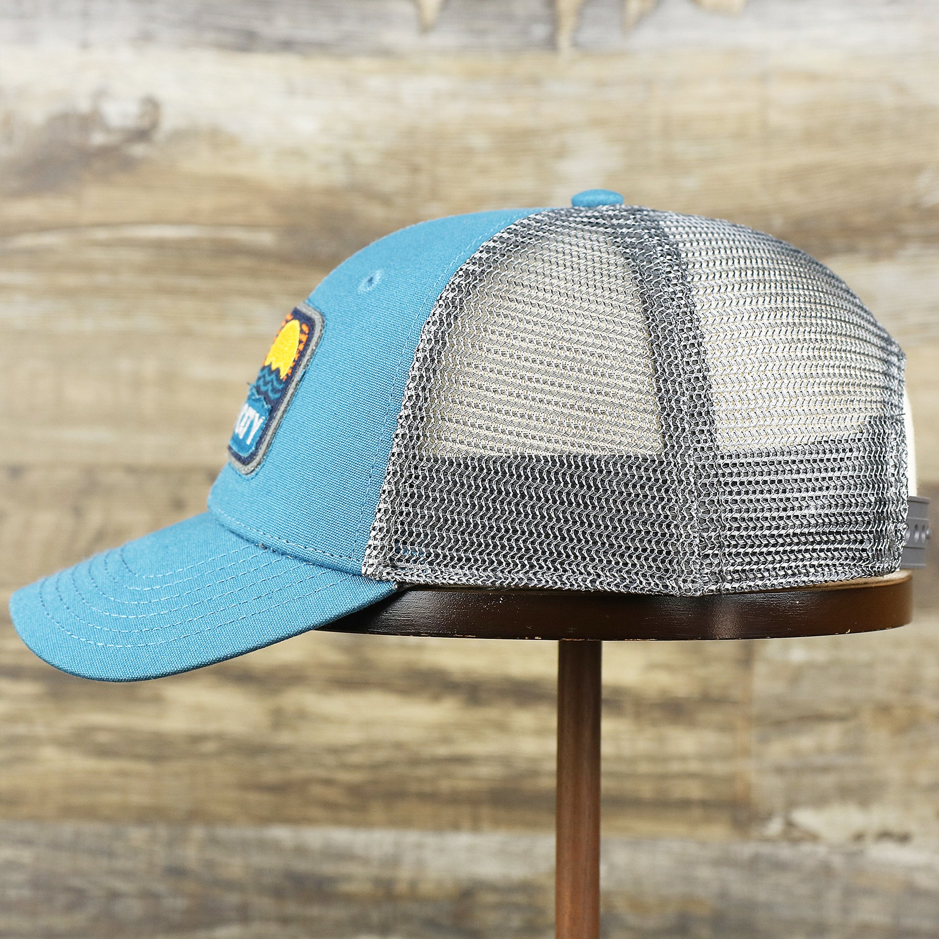 The wearer's left on the Youth New Jersey Ocean City Sunset Mesh Back Trucker Hat | Marine Blue And Dark Gray Mesh Youth Trucker Hat
