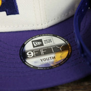 The 9Fifty Sticker on the Youth Los Angeles Lakers NBA 2022 Draft Gray Bottom 9Fifty Snapback | New Era Cream/Purple