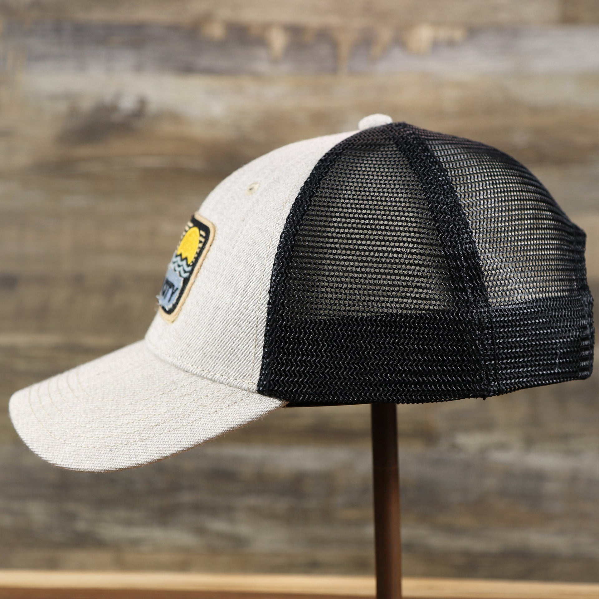 The wearer's left of the New Jersey Ocean City Sunset Mesh Back Trucker Hat | Heather Tan And Black Mesh Trucker Hat