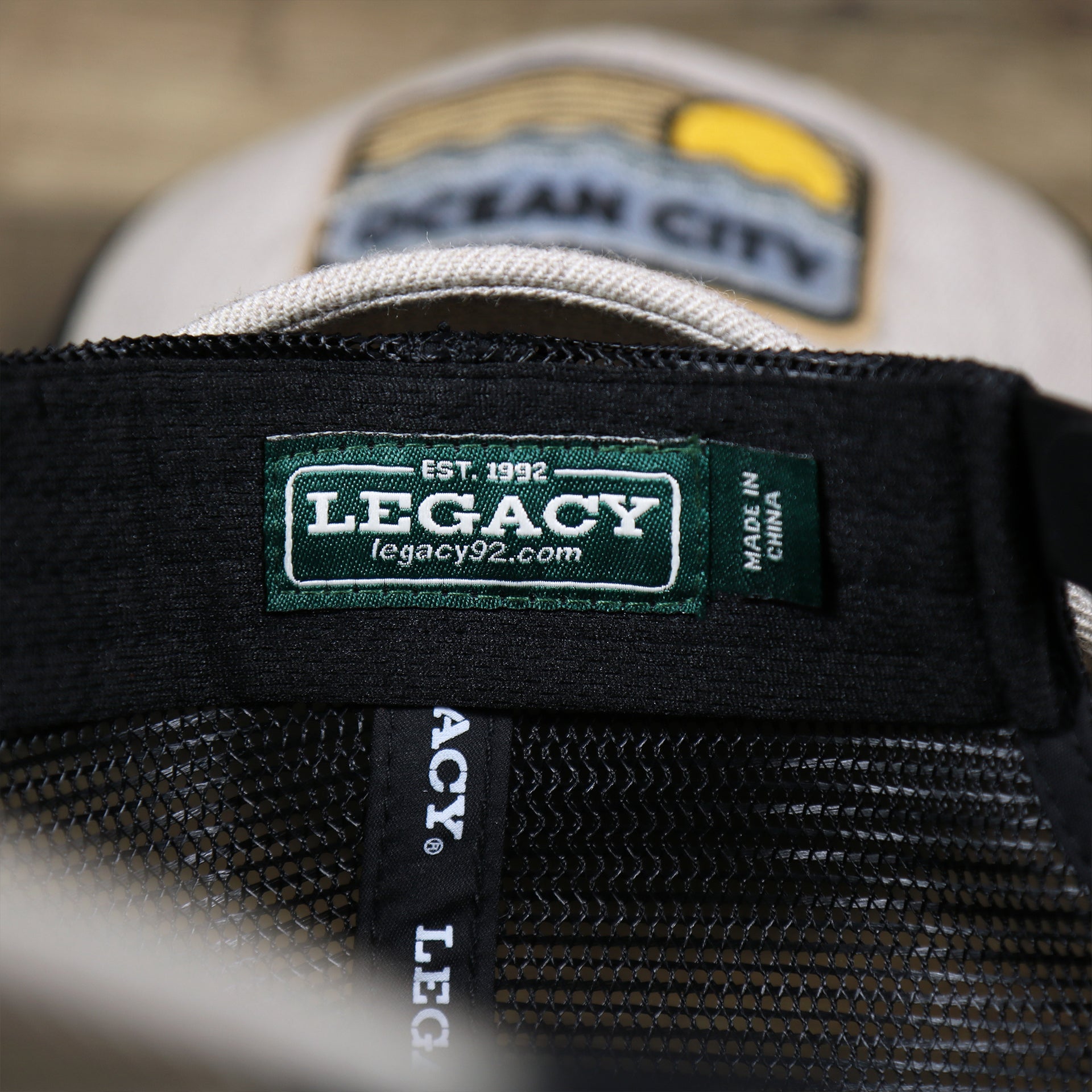 The Legacy Tag on the New Jersey Ocean City Sunset Mesh Back Trucker Hat | Heather Tan And Black Mesh Trucker Hat