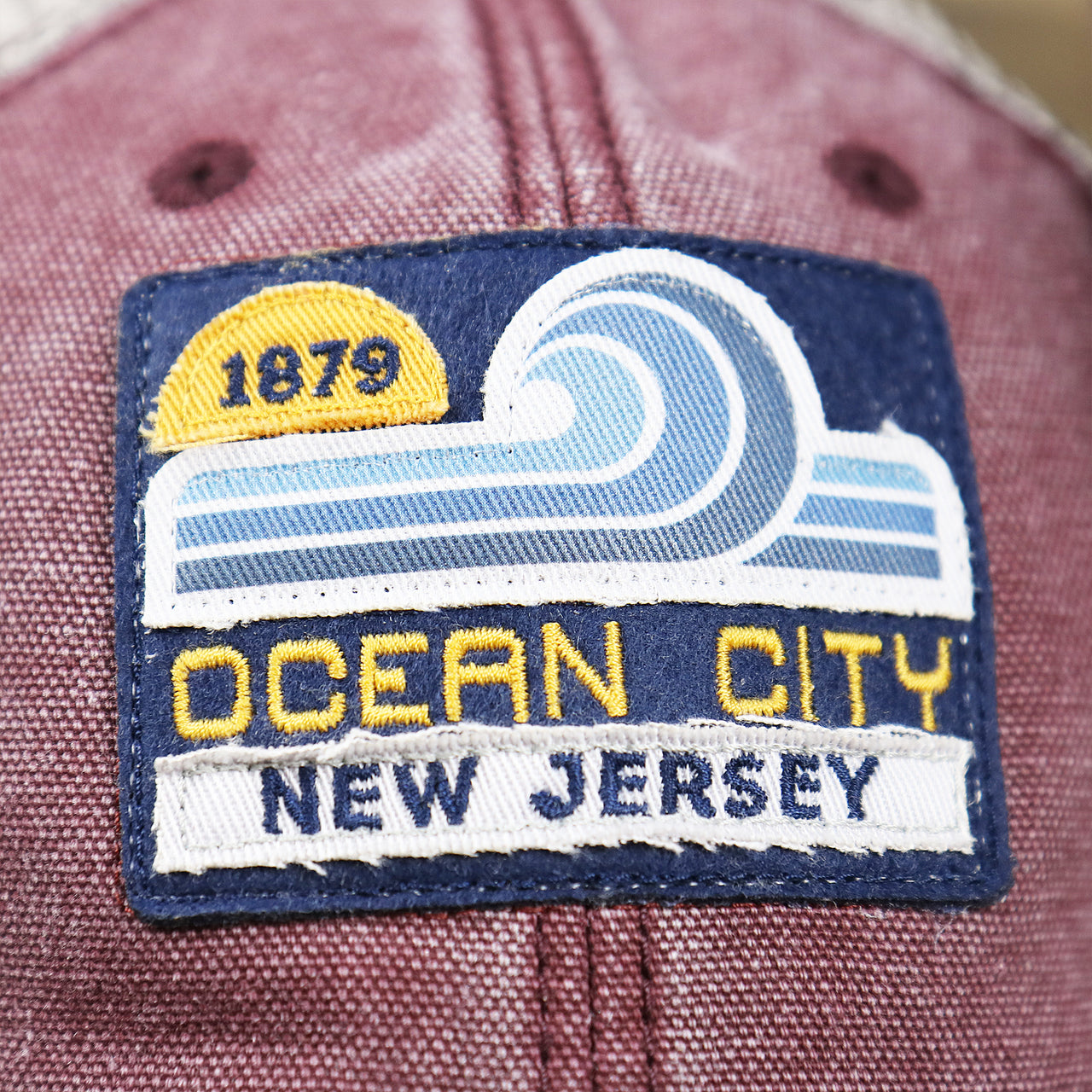 The Ocean City Wave Patch on the OCNJ 1879 Ocean City New Jersey Wave Trucker Hat | Burgundy And Khaki Mesh Trucker Hat