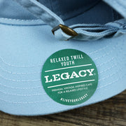 The Youth Legacy Sticker on the Youth Pink OCNJ Wordmark White Outline Dad Hat | Youth Light Blue Dad Hat