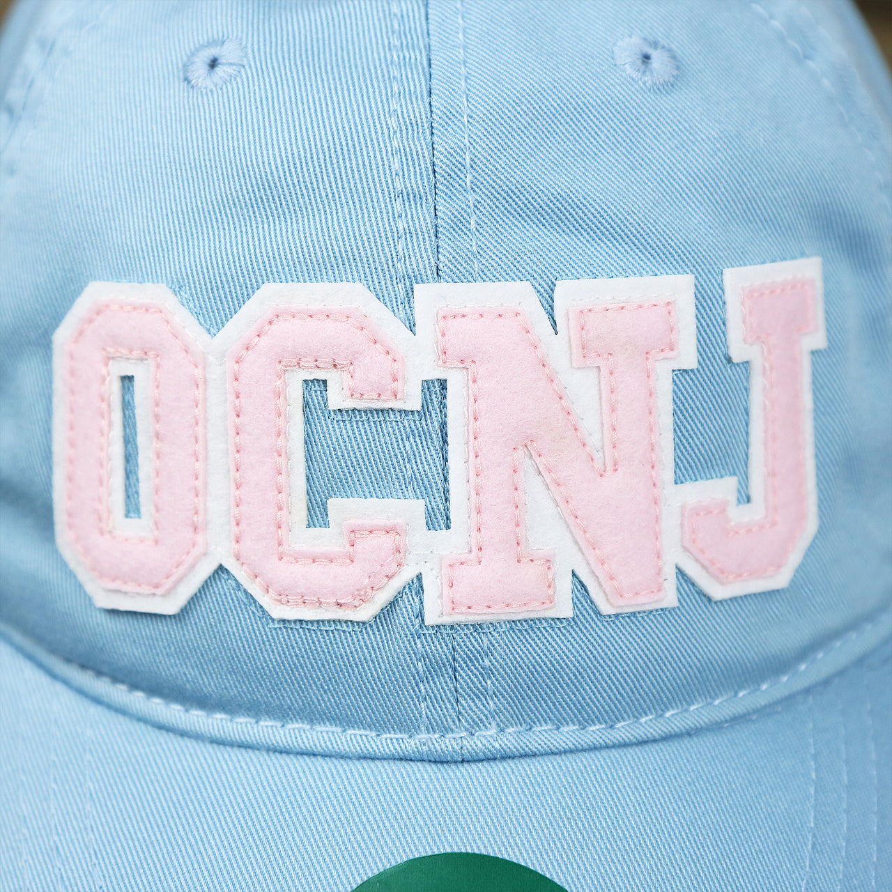 The OCNJ Wordmark on the Pink OCNJ Wordmark White Outline Dad Hat | Light Blue Dad Hat