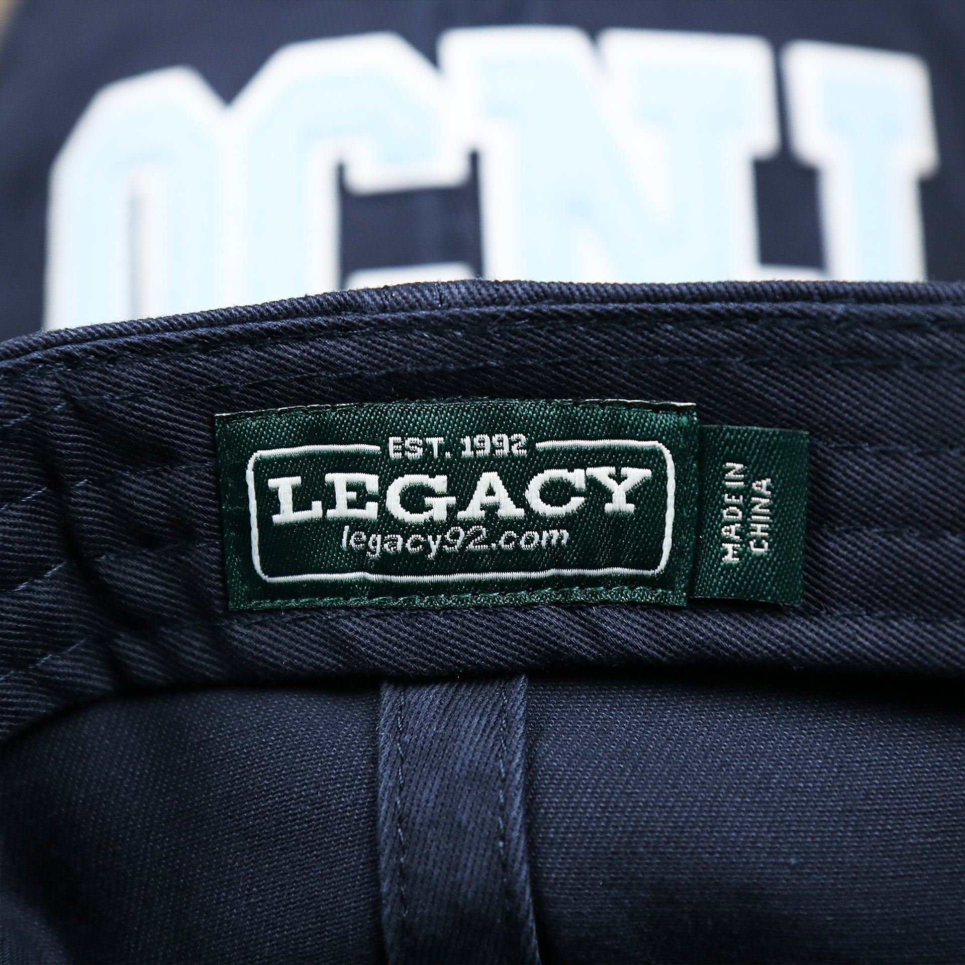 The Legacy Tag on the Youth Light Blue OCNJ Wordmark White Outline Dad Hat | Youth Navy Blue Dad Hat