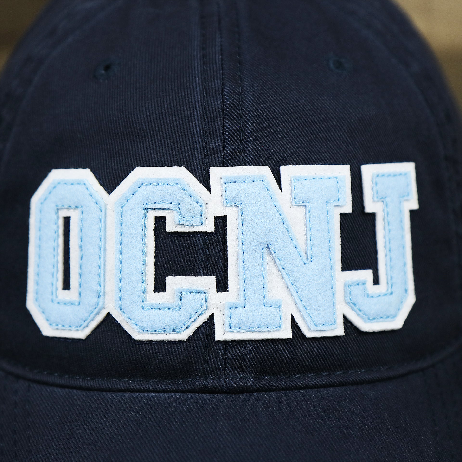 The OCNJ Wordmark on the Youth Light Blue OCNJ Wordmark White Outline Dad Hat | Youth Navy Blue Dad Hat