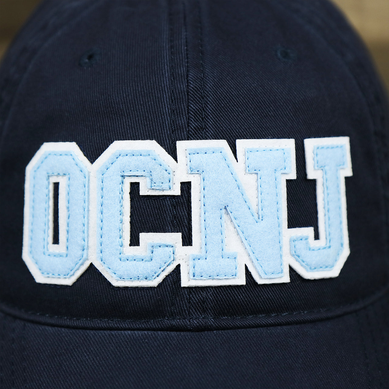 The OCNJ Wordmark on the Light Blue OCNJ Wordmark White Outline Dad Hat | Navy Blue Dad Hat