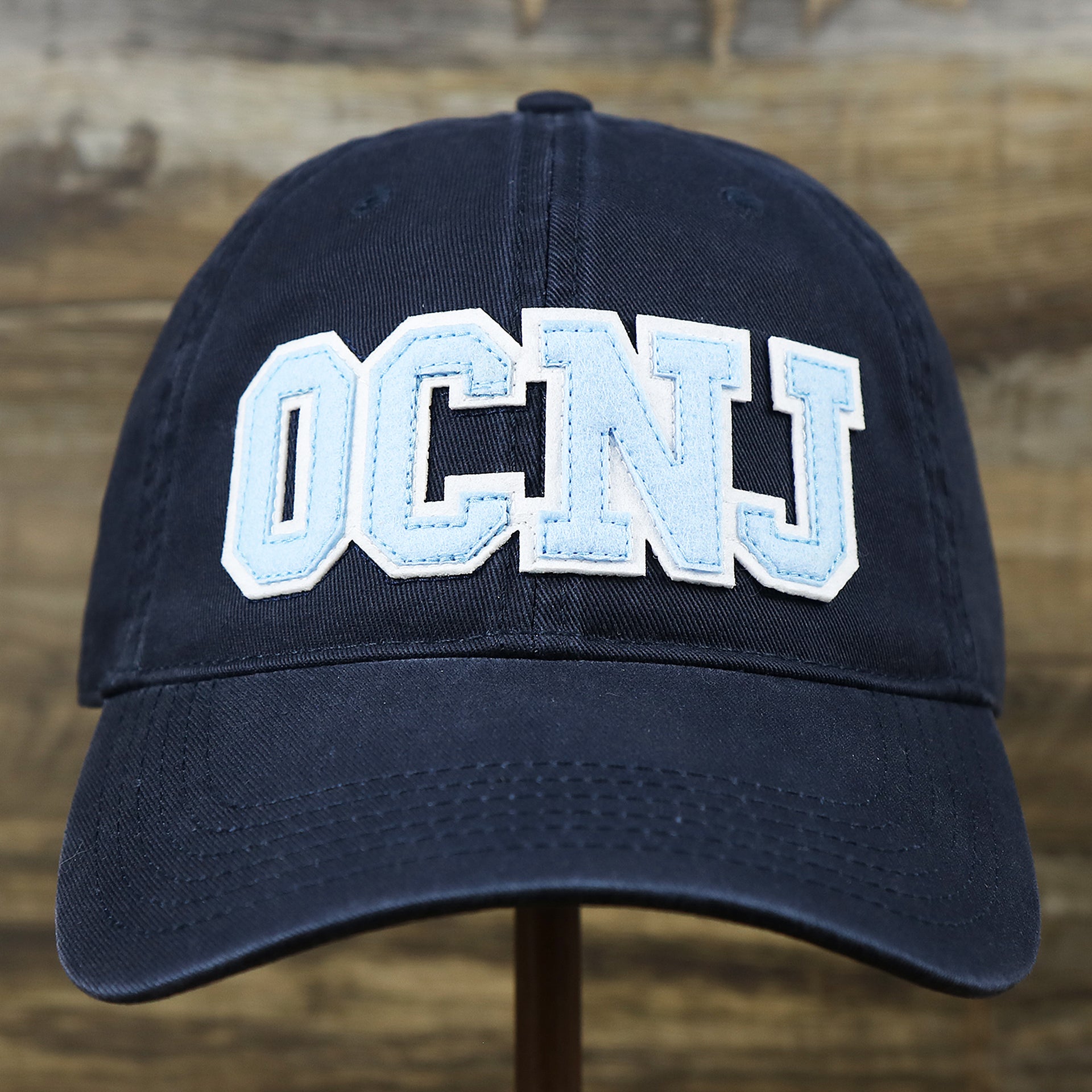 The front of the Youth Light Blue OCNJ Wordmark White Outline Dad Hat | Youth Navy Blue Dad Hat
