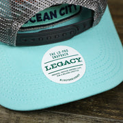 The Legacy Sticker on the New Jersey Ocean City Sunset Mesh Back Trucker Hat | Tahiti Blue And Grey Mesh Trucker Hat