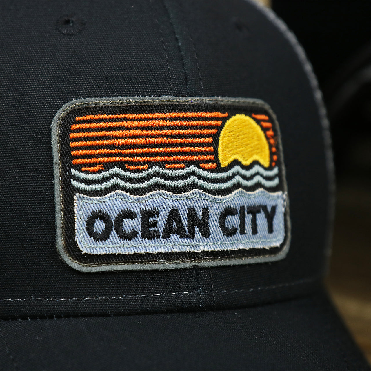 The OC Sunset Patch on the Youth New Jersey Ocean City Sunset Mesh Back Trucker Hat | Tahiti Blue And Grey Mesh Trucker Hat