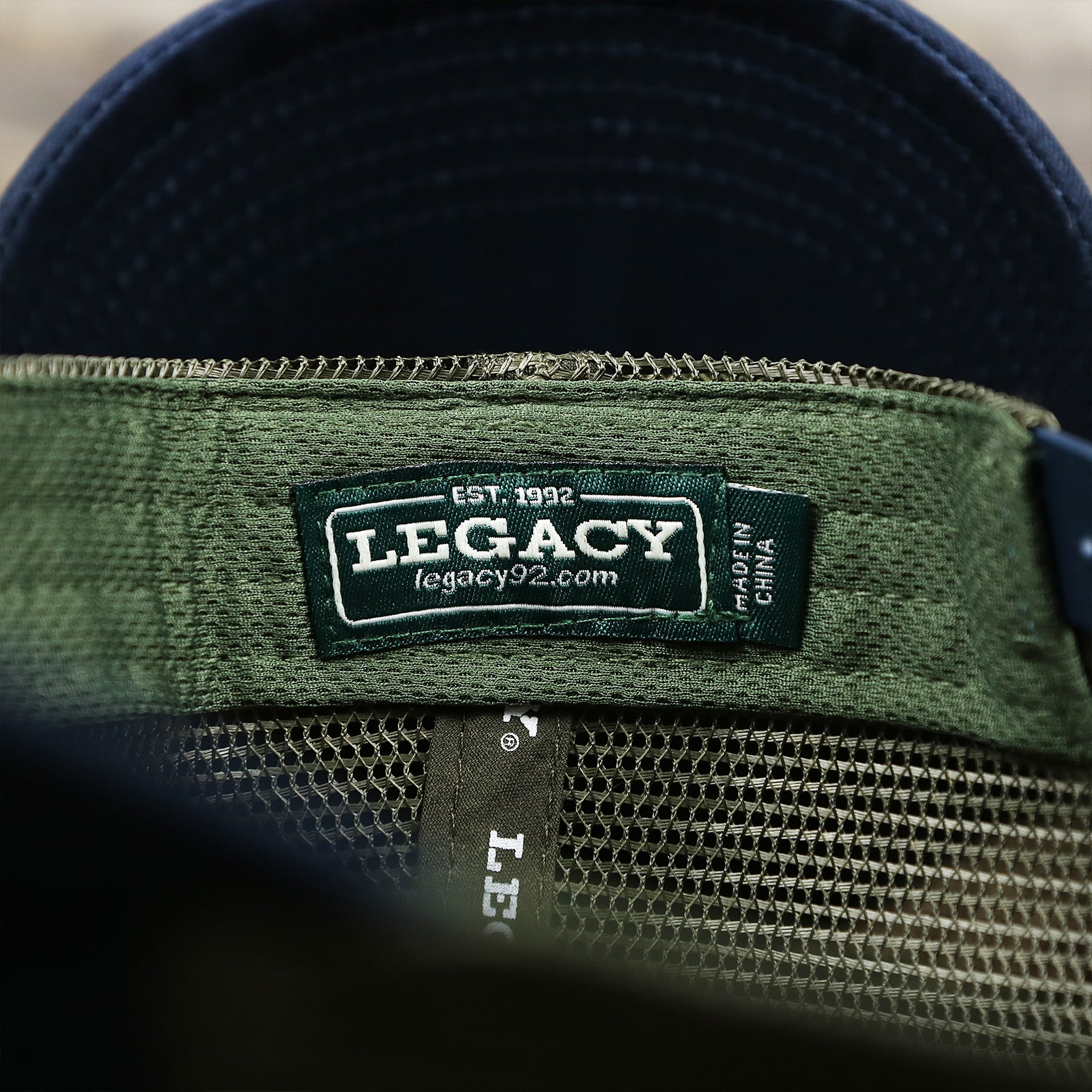 The Legacy Tag on the New Jersey Ocean City Sunset Mesh Back Trucker Hat | Navy Blue And Olive Mesh Trucker Hat