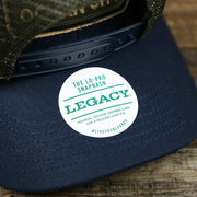 The Legacy Sticker on the New Jersey Ocean City Sunset Mesh Back Trucker Hat | Navy Blue And Olive Mesh Trucker Hat