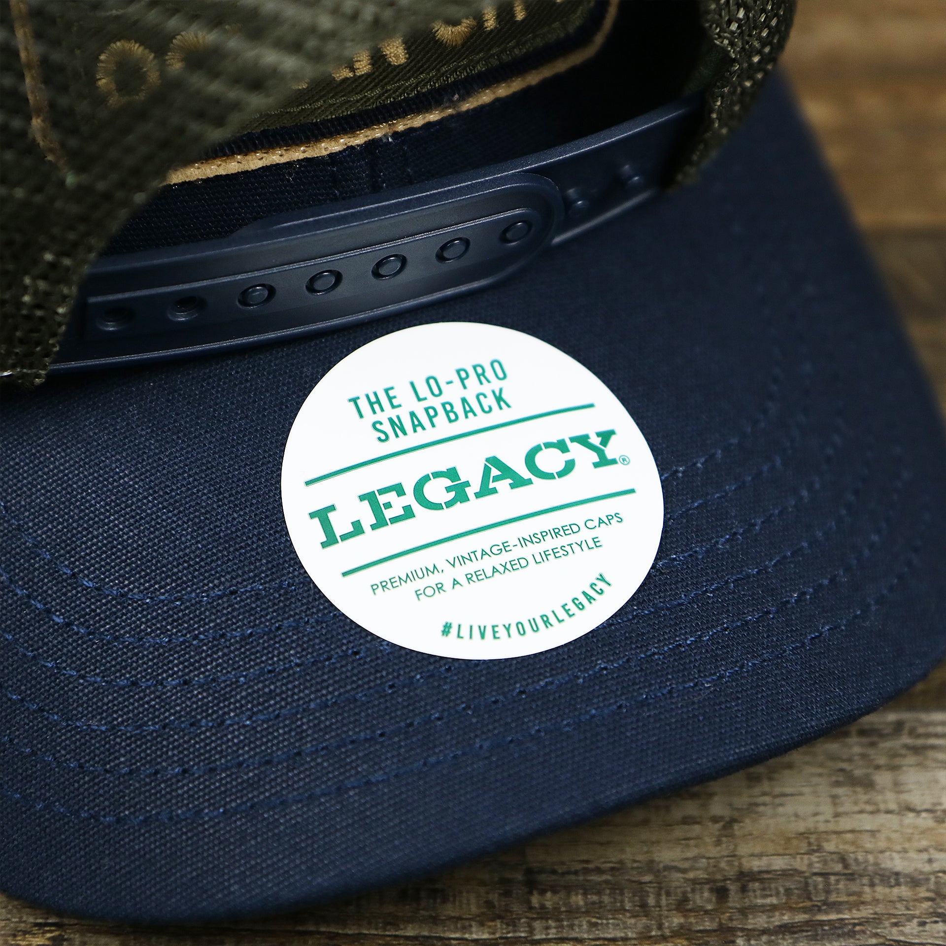 The Legacy Sticker on the New Jersey Ocean City Sunset Mesh Back Trucker Hat | Navy Blue And Olive Mesh Trucker Hat