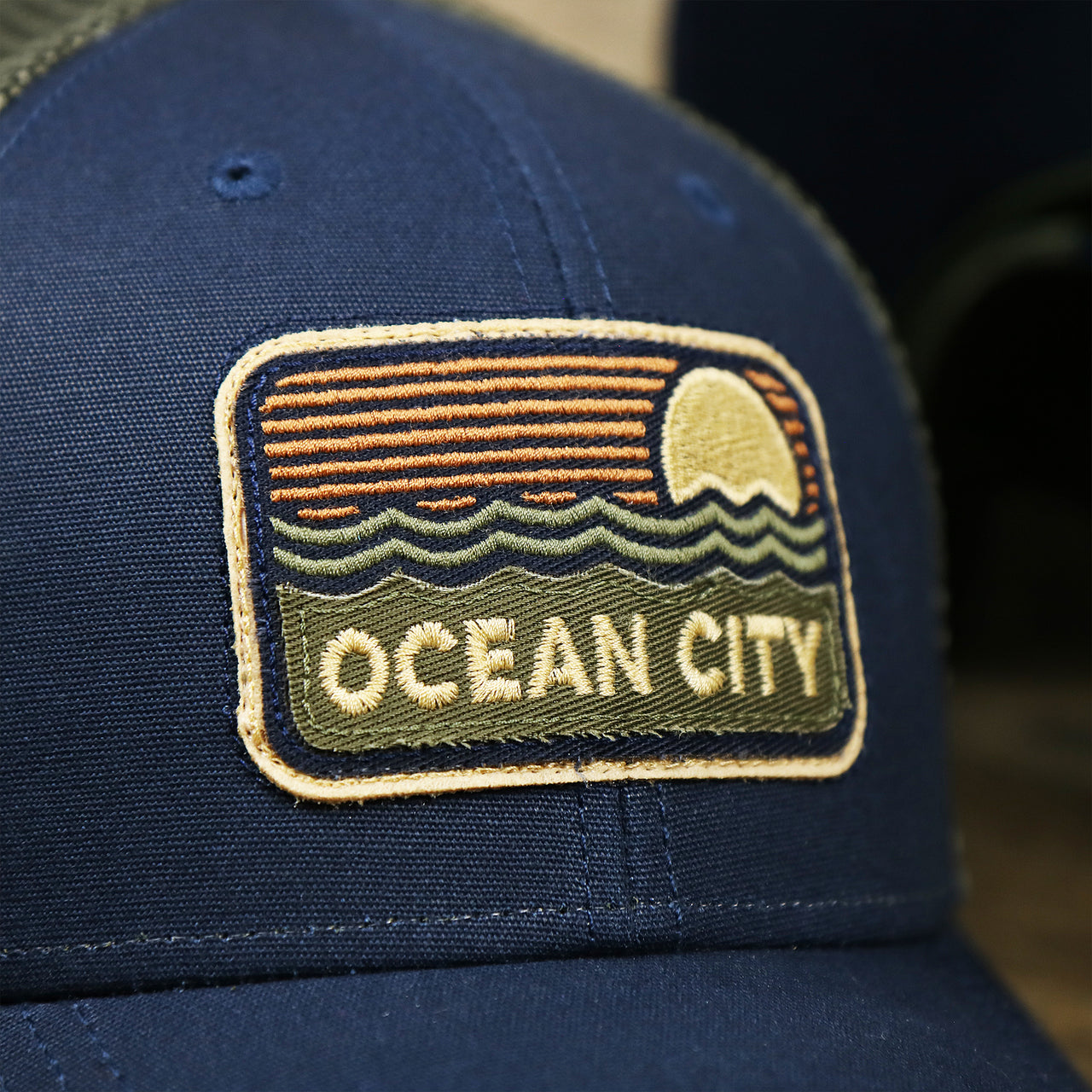 The OC Sunset Patch on the New Jersey Ocean City Sunset Mesh Back Trucker Hat | Navy Blue And Olive Mesh Trucker Hat