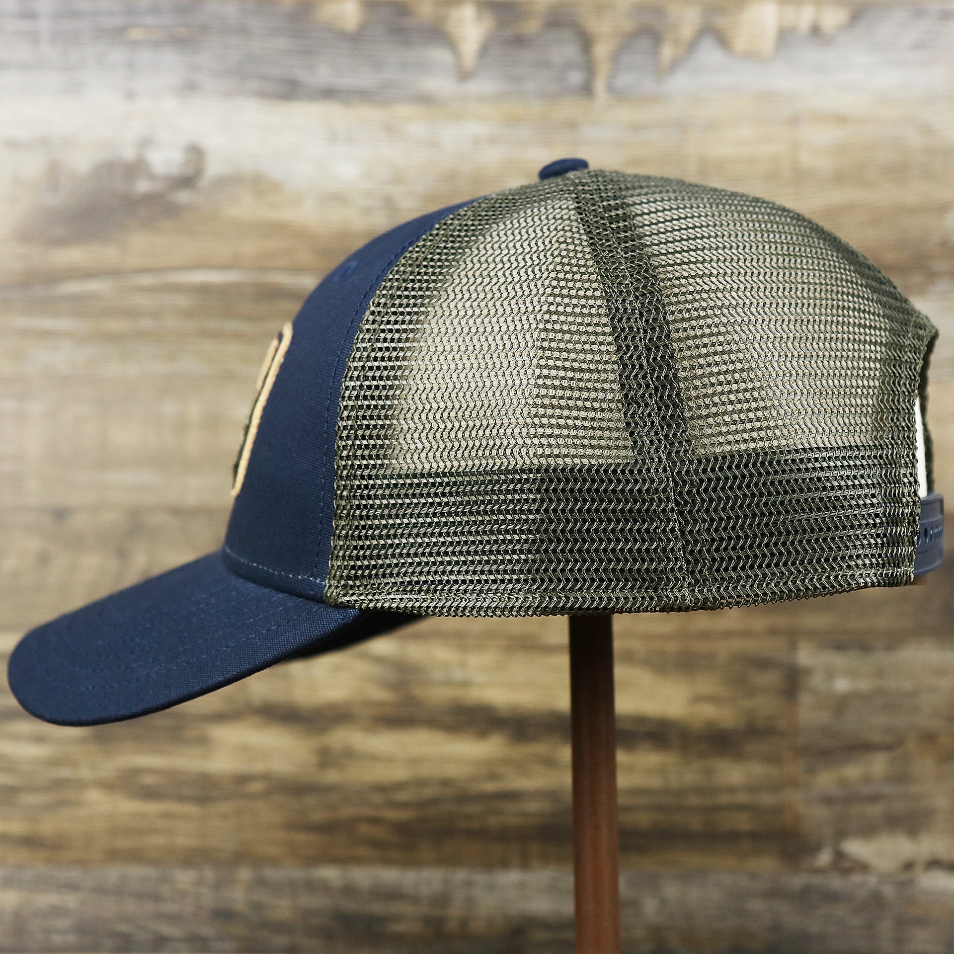 The wearer's left on the New Jersey Ocean City Sunset Mesh Back Trucker Hat | Navy Blue And Olive Mesh Trucker Hat