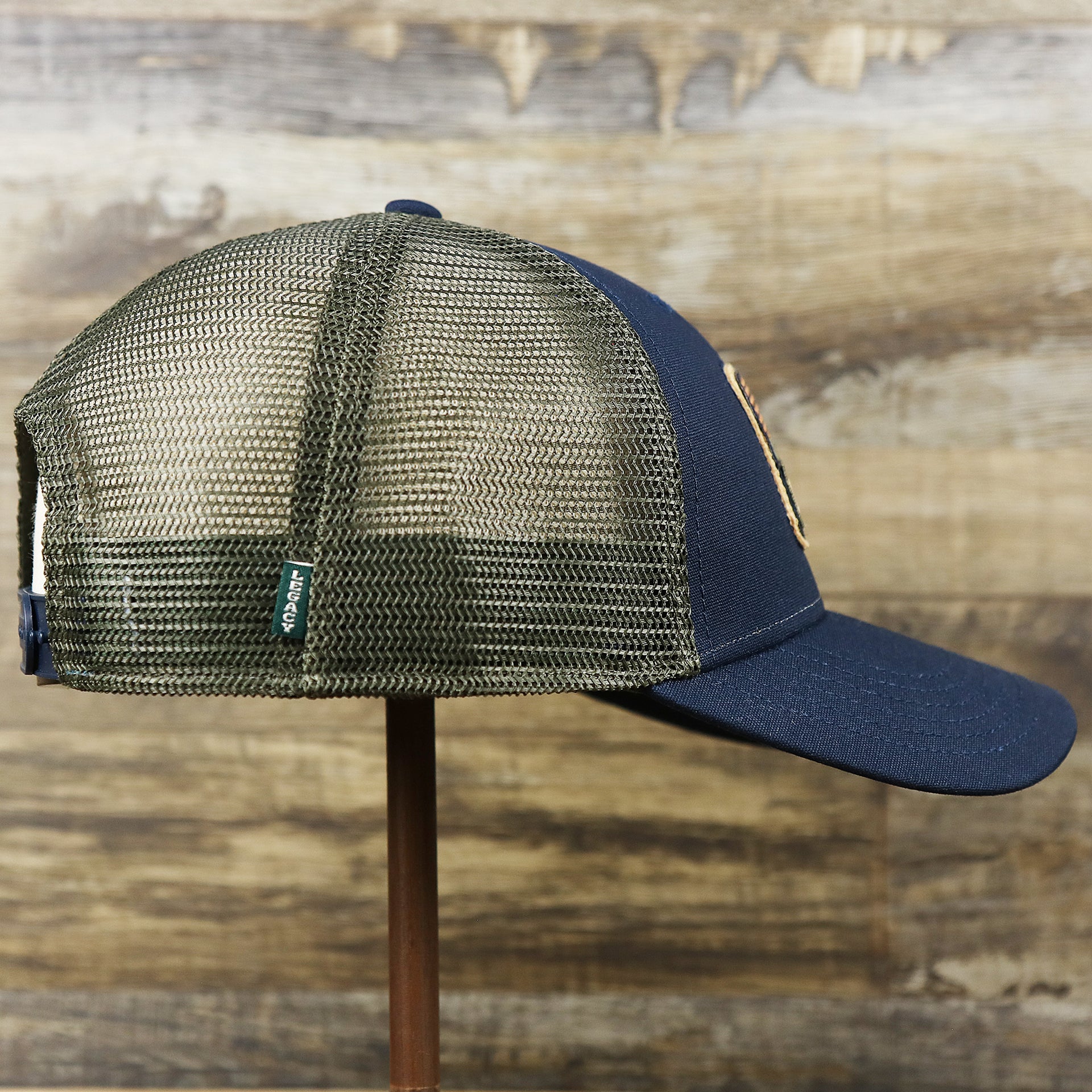 The wearer's right on the New Jersey Ocean City Sunset Mesh Back Trucker Hat | Navy Blue And Olive Mesh Trucker Hat