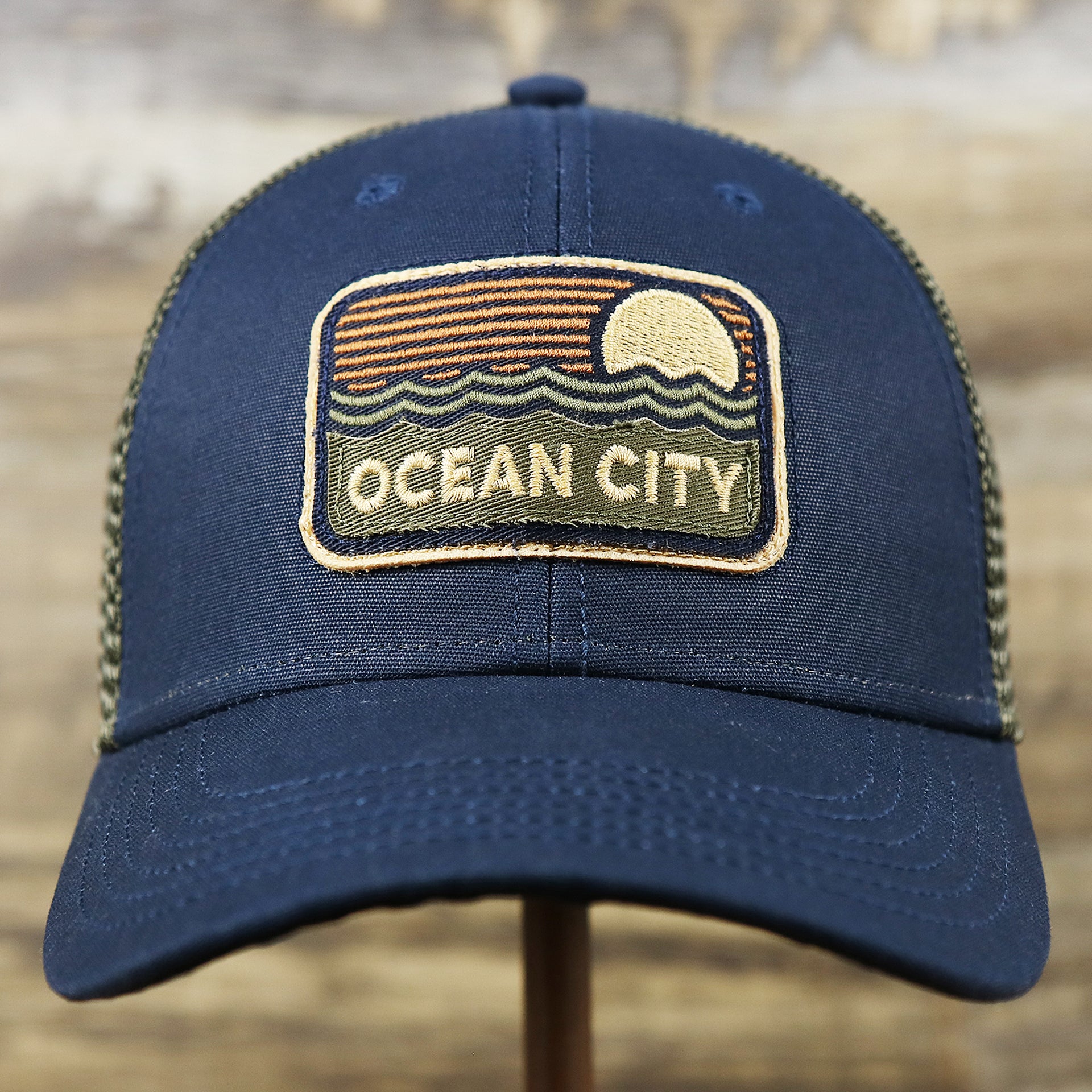 The front of the New Jersey Ocean City Sunset Mesh Back Trucker Hat | Navy Blue And Olive Mesh Trucker Hat