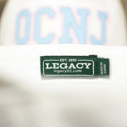 The Legacy Tag on the Youth Light Blue OCNJ Wordmark Pink Outline Dad Hat | Youth White Dad Hat