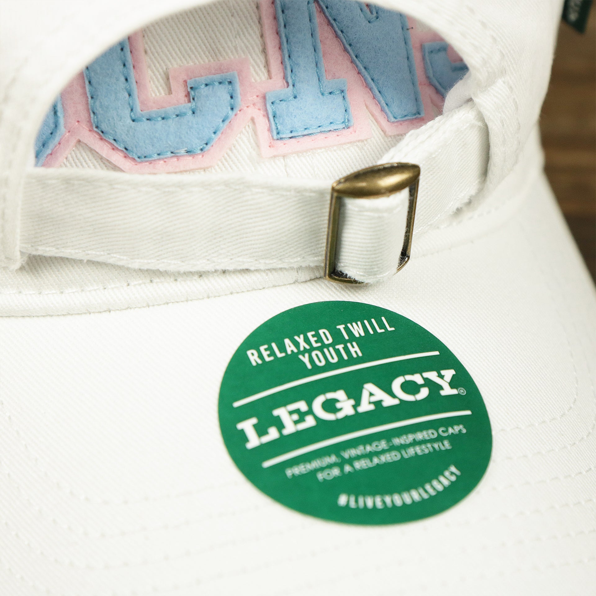 The Legacy Youth Sticker on the Youth Light Blue OCNJ Wordmark Pink Outline Dad Hat | Youth White Dad Hat