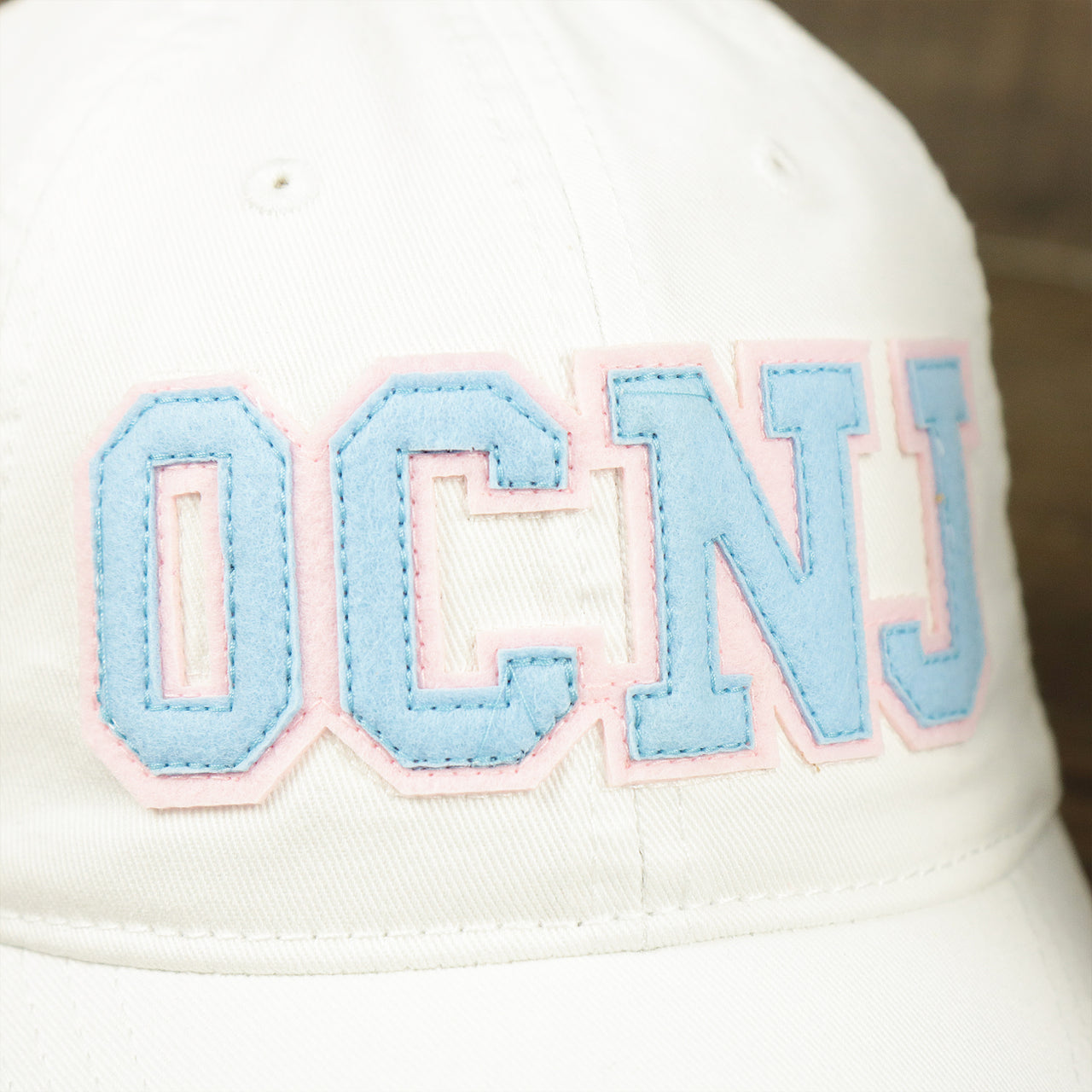 The OCNJ Wordmark on the Youth Light Blue OCNJ Wordmark Pink Outline Dad Hat | Youth White Dad Hat