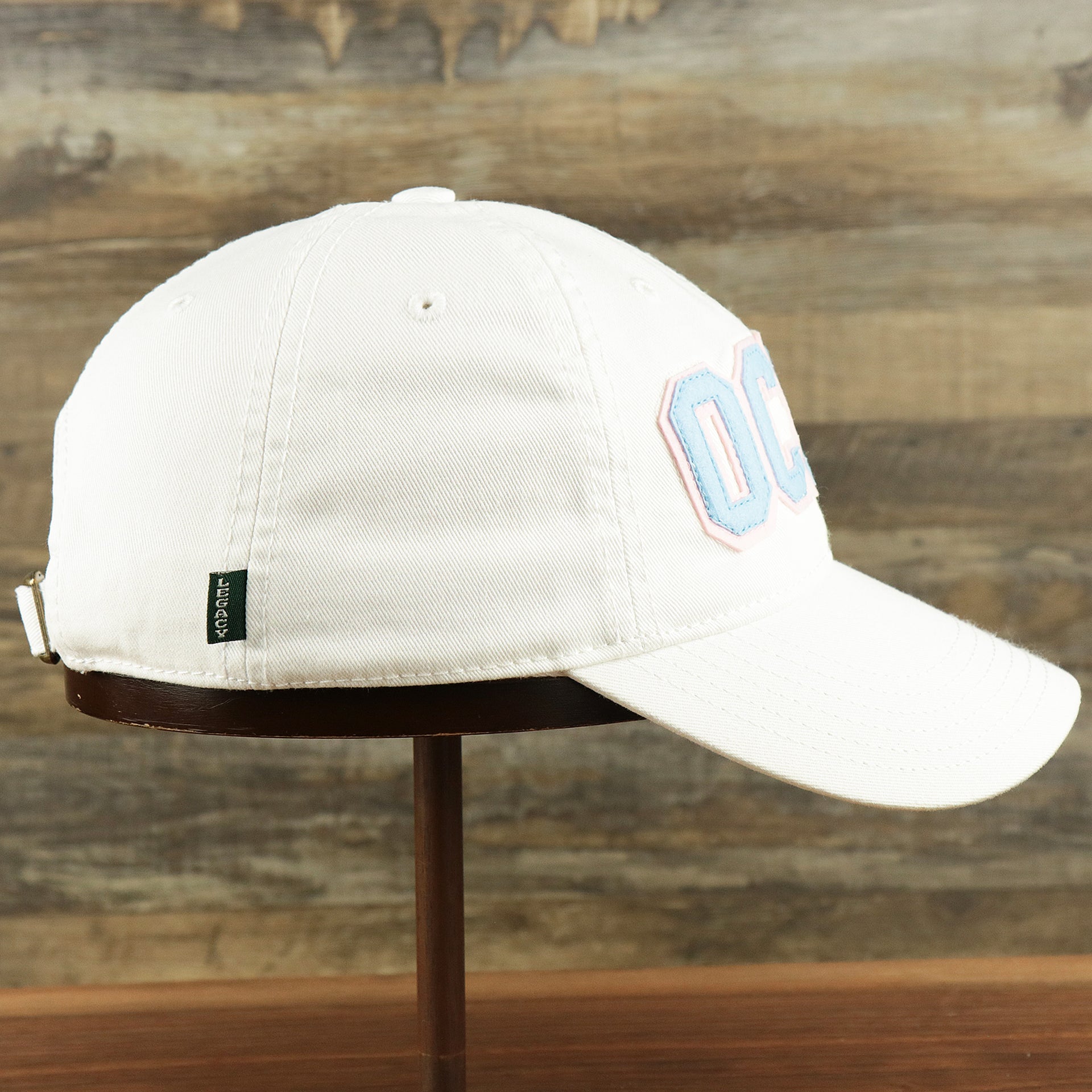 The wearer's right on the Youth Light Blue OCNJ Wordmark Pink Outline Dad Hat | Youth White Dad Hat