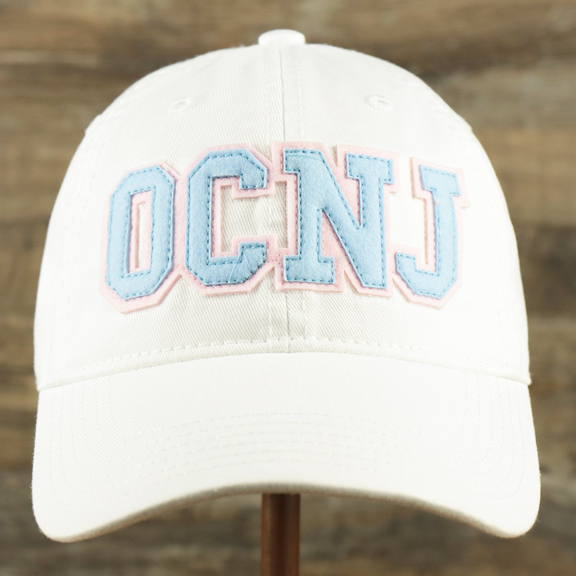 The front of the Youth Light Blue OCNJ Wordmark Pink Outline Dad Hat | Youth White Dad Hat