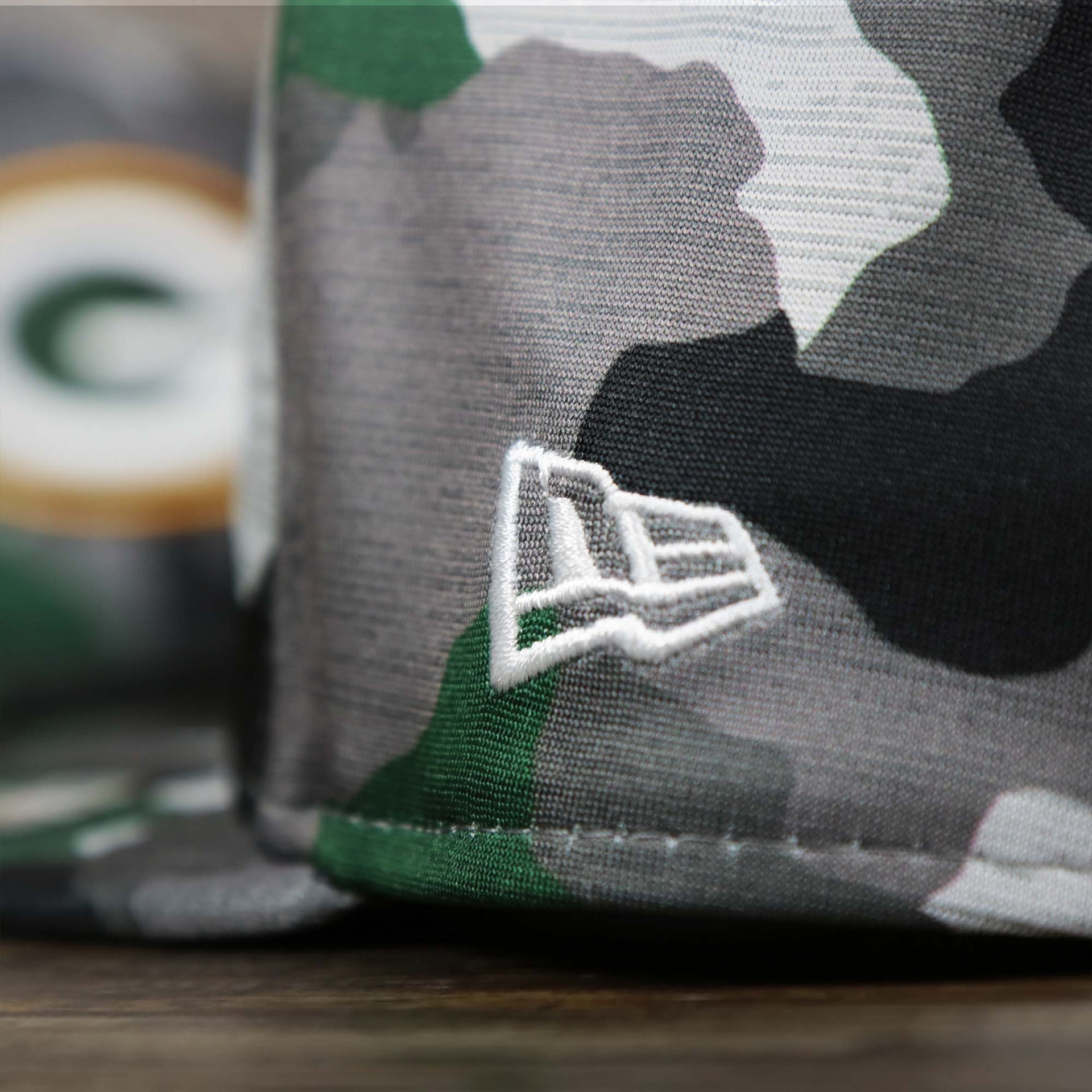 A close up of the New Era Logo on the Green Bay Packers NFL OnField Summer Training 2022 Camo 9Fifty Snapback | Green Camo 9Fifty