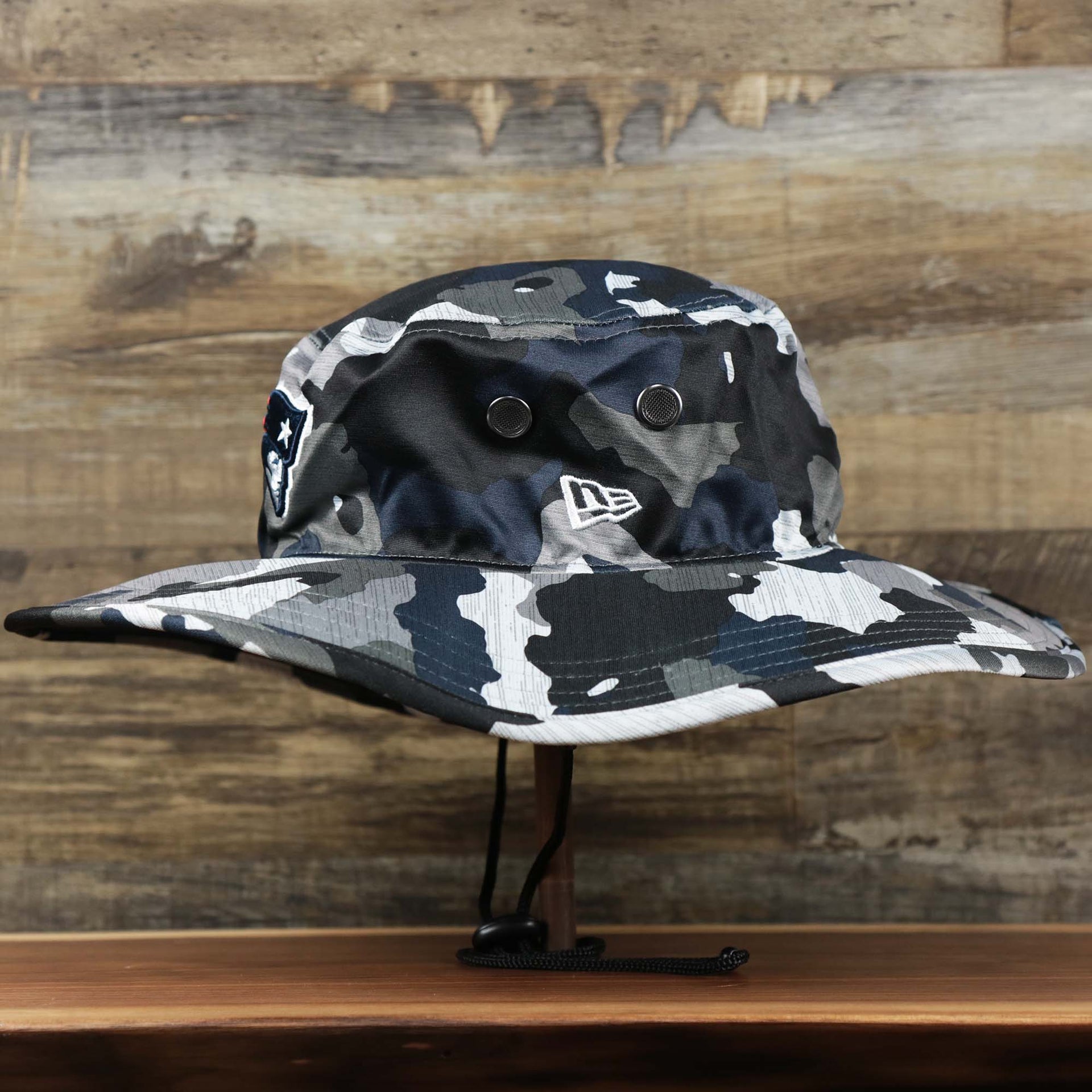 The wearer's left on the New England Patriots NFL Summer Training Camp 2022 Camo Bucket Hat | Navy Bucket Hat