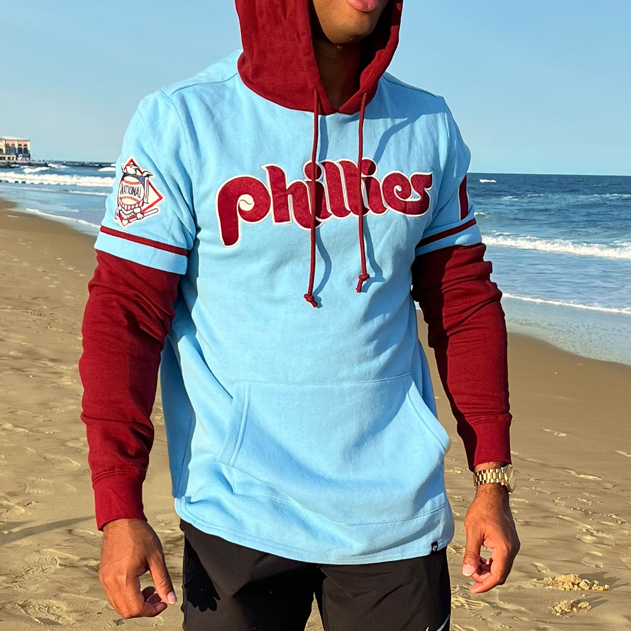 The front of the Cooperstown Philadelphia Phillies Wordmark Retro Phillies Colorway Trifecta Shortstop Layered Hoodie With MLB Side Patch | Carolina Blue And Maroon Pullover Hoodie