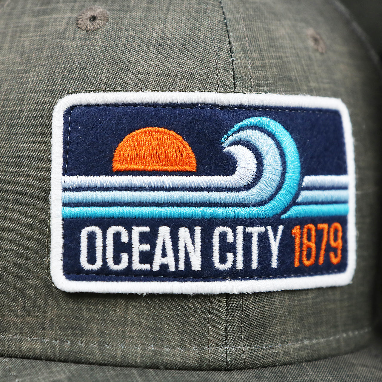 The Ocean City Sunset Wave Patch on the OCNJ Ocean City 1879 Sunset Wave Logo Mesh Stretch FIt Hat | Dark Green And Dark Grey Stretch Fit Hat