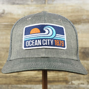 The front of the OCNJ Ocean City 1879 Sunset Wave Logo Mesh Stretch FIt Hat | Dark Green And Dark Grey Stretch Fit Hat