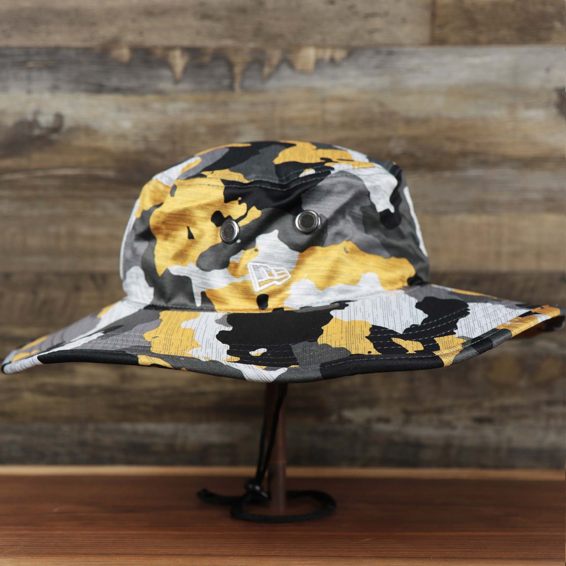 The wearer's left on the Pittsburgh Steelers NFL Summer Training Camp 2022 Camo Bucket Hat | Yellow Bucket Hat
