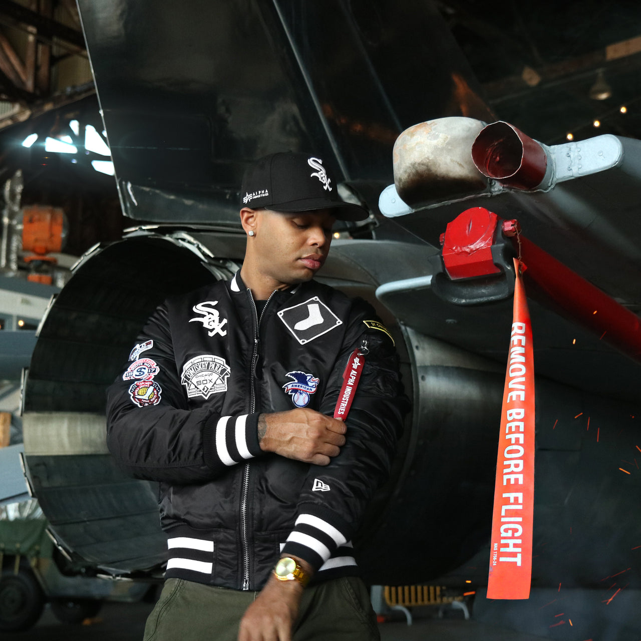 The Chicago White Sox MLB Patch Alpha Industries Reversible Bomber Jacket With Camo Liner | Black Bomber Jacket in front of a jet