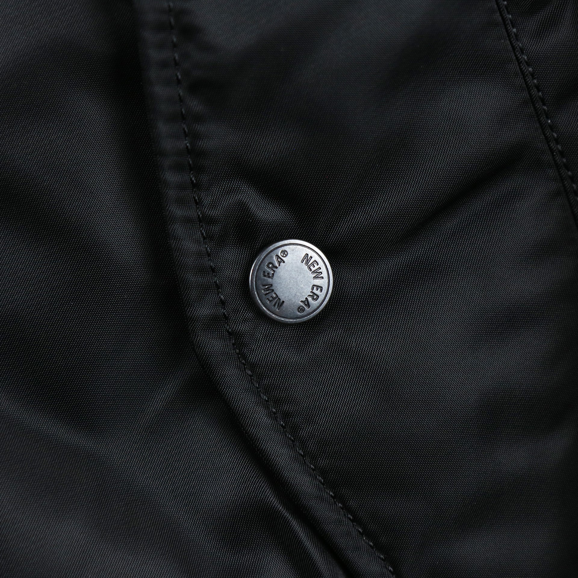 A close up of the custom metal buttons with New Era Wordmark on the Chicago White Sox MLB Patch Alpha Industries Reversible Bomber Jacket With Camo Liner | Black Bomber Jacket