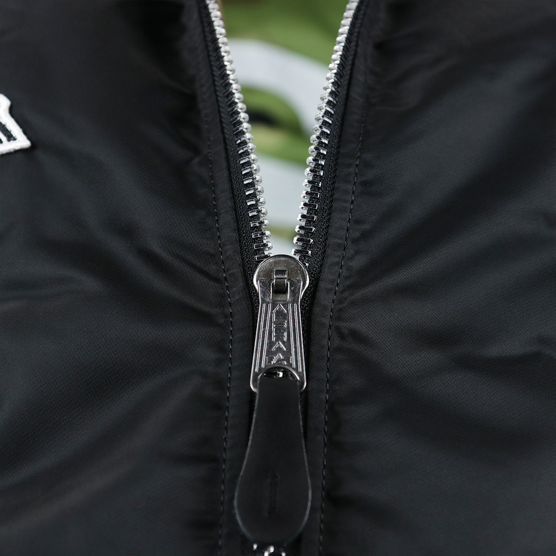 A close up of the zipper with Alpha engraved on the Chicago White Sox MLB Patch Alpha Industries Reversible Bomber Jacket With Camo Liner | Black Bomber Jacket