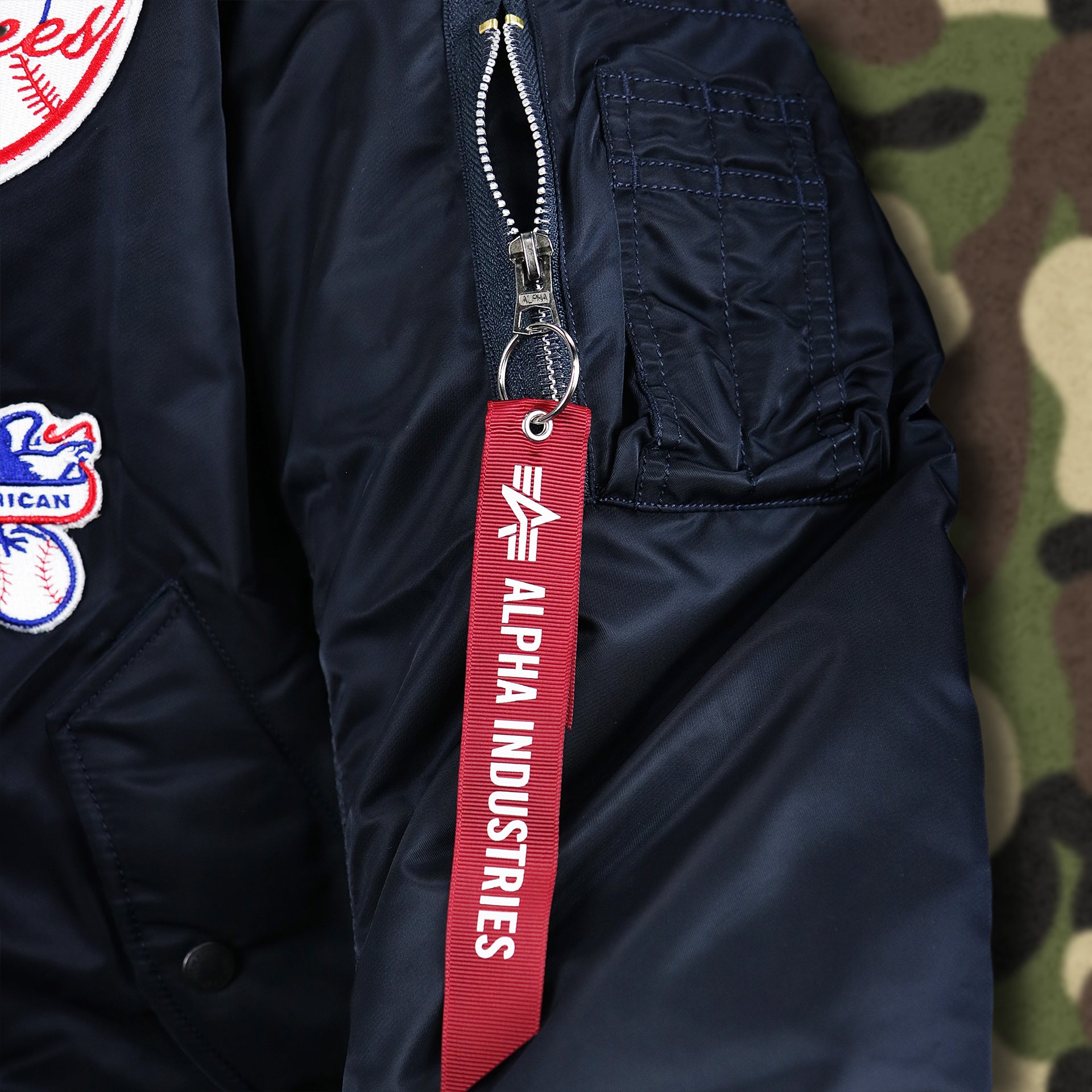 The Alpha Industries Flight Tag on the New York Yankees MLB Patch Alpha Industries Reversible Bomber Jacket With Camo Liner | Navy Blue Bomber Jacket