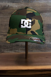 the front of the Camouflage Print Skater Hat | DC Shoes Black Bottom Camo Flexfit Cap has a large white DC Shoes logo on the front