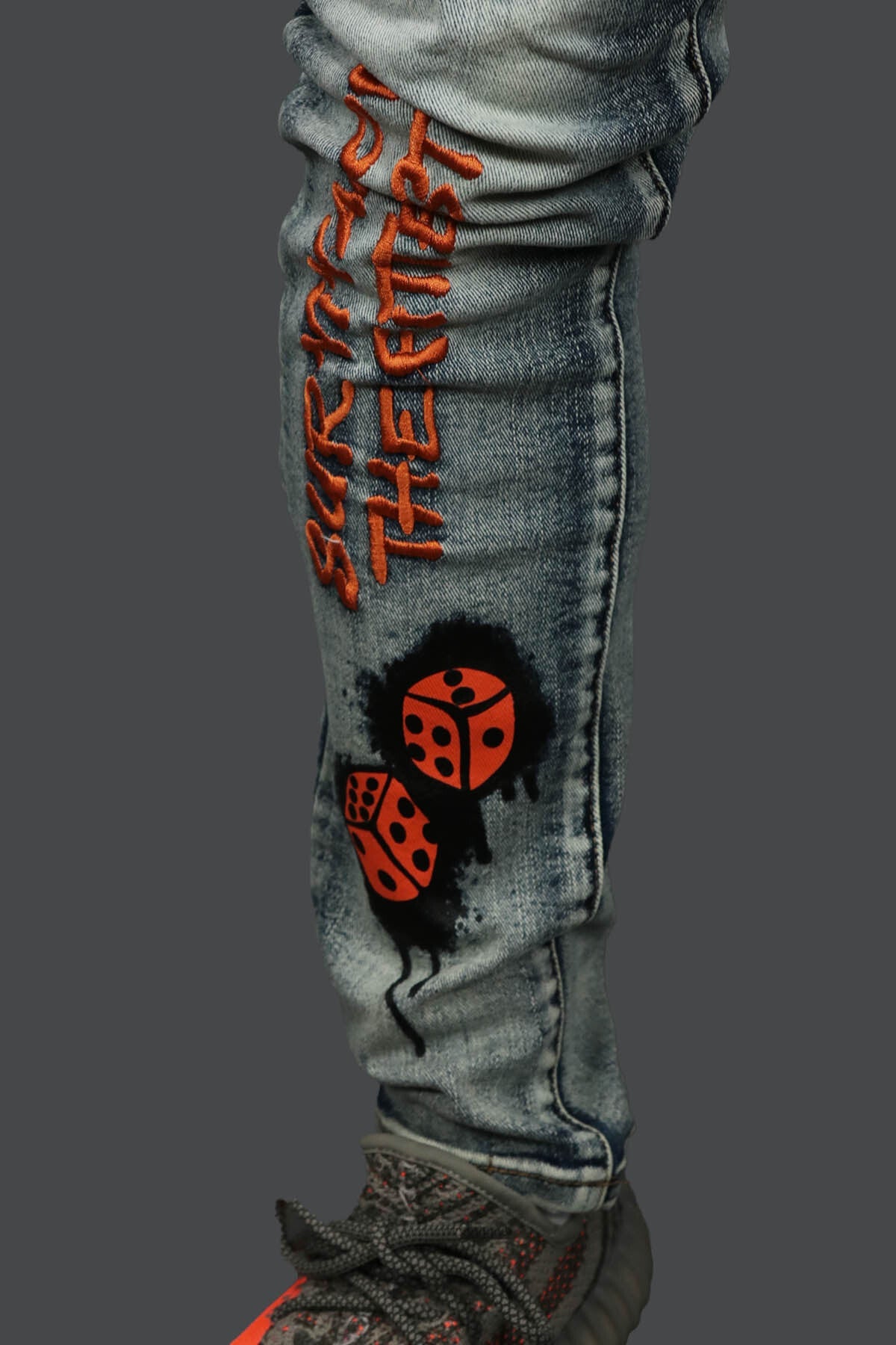 A close up of the custom graphic and words embroidered in ornage on the Only The Strong Custom Spray Painted Distressed Denim Pants Motive Denim | Vintage |  